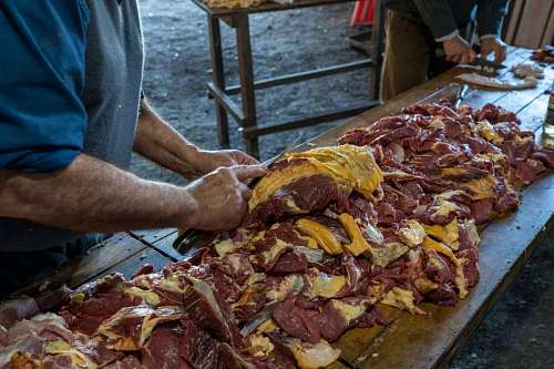 asado Un hombre cortando carne recien faenada con su cuchillo en el campo
