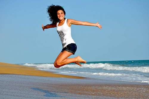 disfrutando Mujer joven en la playa saltando con los brazos abiertos