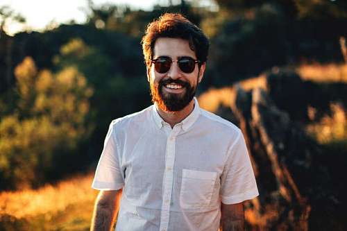 Hombre joven con camisa blanca y lentes mirando a la camara y sonriendo