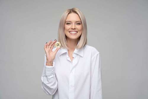 Mujer sonriendo con moneda de bitcoin en la mano