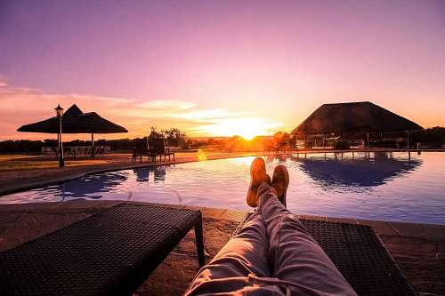 recreativo Hombre recostado en una reposera frente a una piscina al atardecer