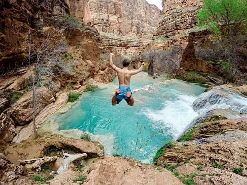 Joven saltando al interior de un rio de montaña