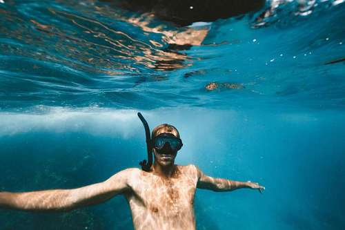 Hombre con mascara de snorkel bajo el agua mirando a la camara