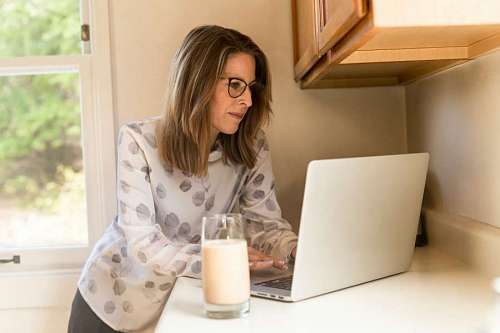 educacion mujer adulta usa su laptop en la alacena mientras toma un vaso de leche