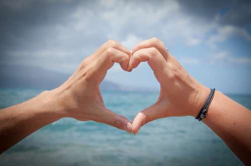 forma de corazon Manos de hombre formando un  corazón en la playa 