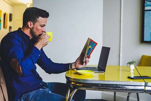 joven desayuna mientras lee un libro frente a su laptop